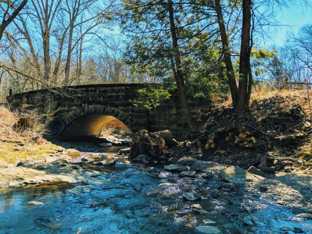 low stone arch bridge over a creek, framed by trees 