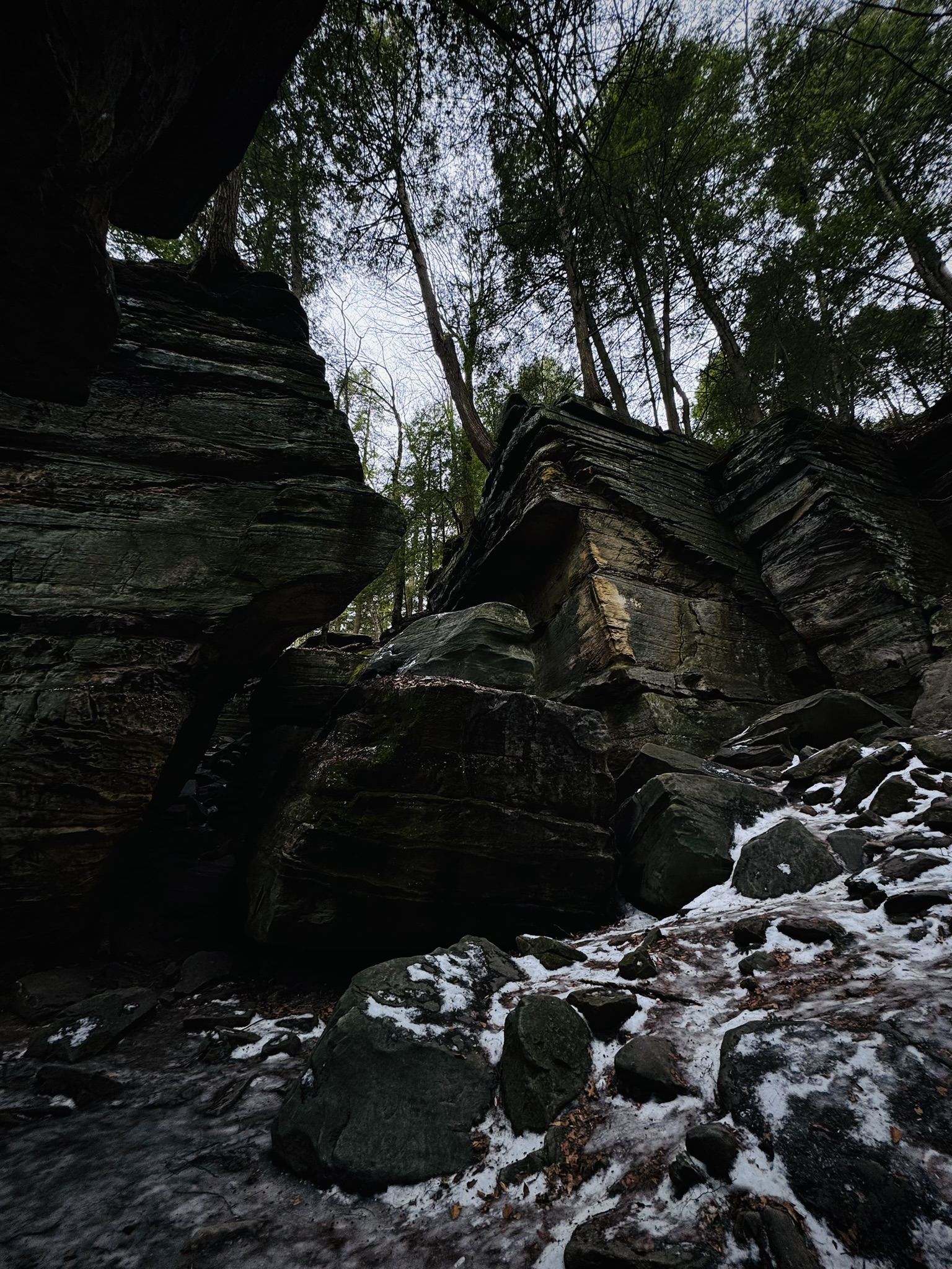 a couple large ledges with hemlock trees growing on top. The smaller boulders in the foreground are all icy and snowy.